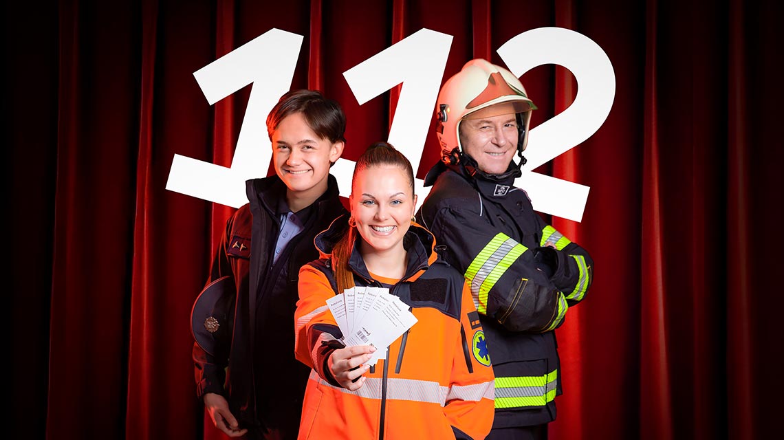 Three emergency responders (paramedic, nurse, and firefighter) stand before a large '112' backdrop, smiling; the paramedic holds several tickets toward the camera.